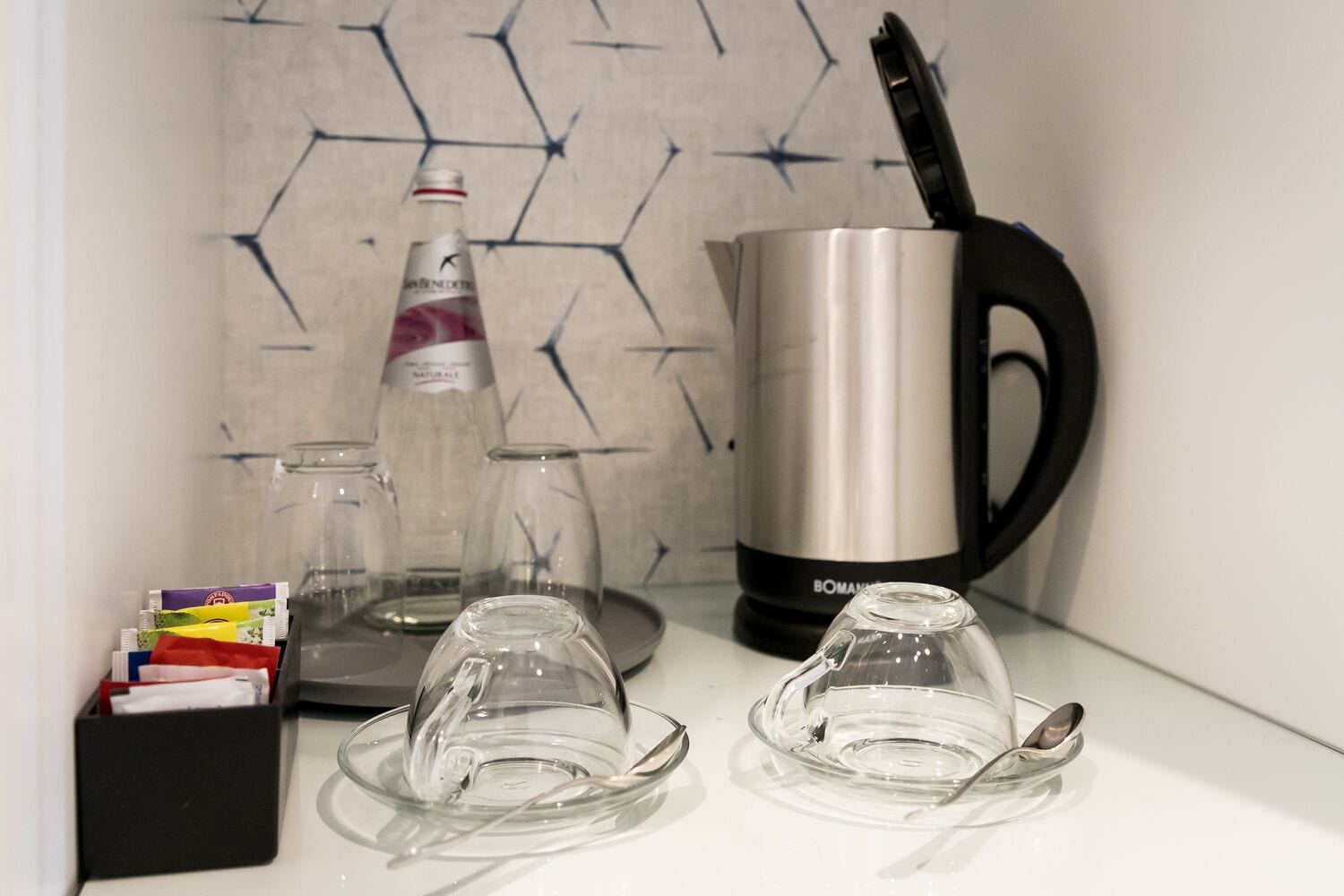 Una encimera de cocina con una cafetera, una botella de agua y dos vasos de vidrio vacíos.