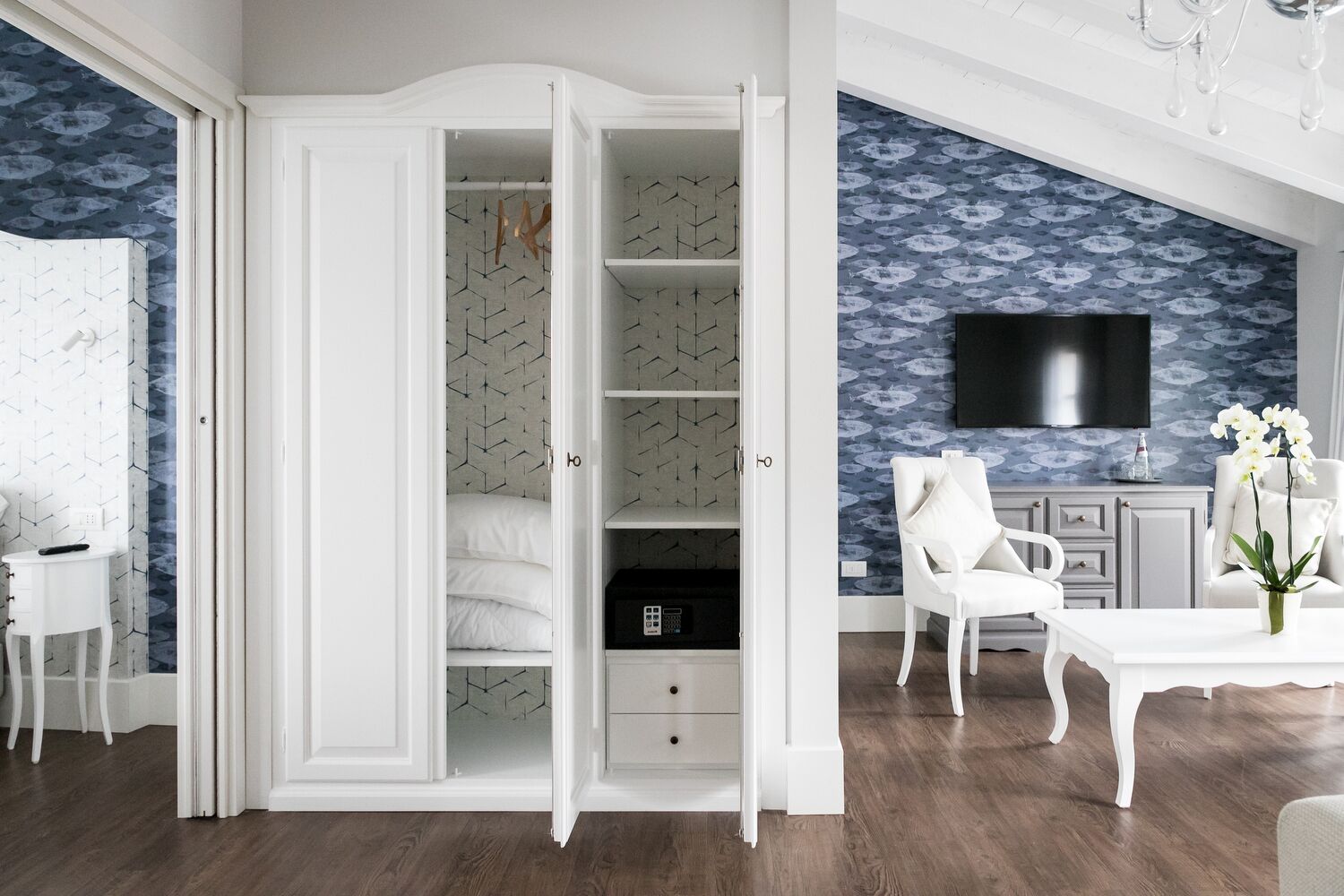 A spacious room with a large walk-in closet, a flat-screen TV mounted on the wall, and a white chair with a vase of flowers.