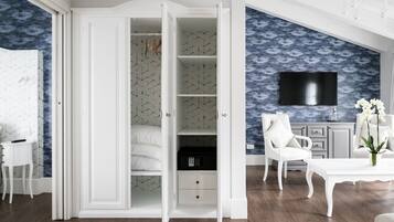 Ruime kamer met een grote inloopkast, een flatscreen televisie aan de wand en een witte stoel met een bloevas.