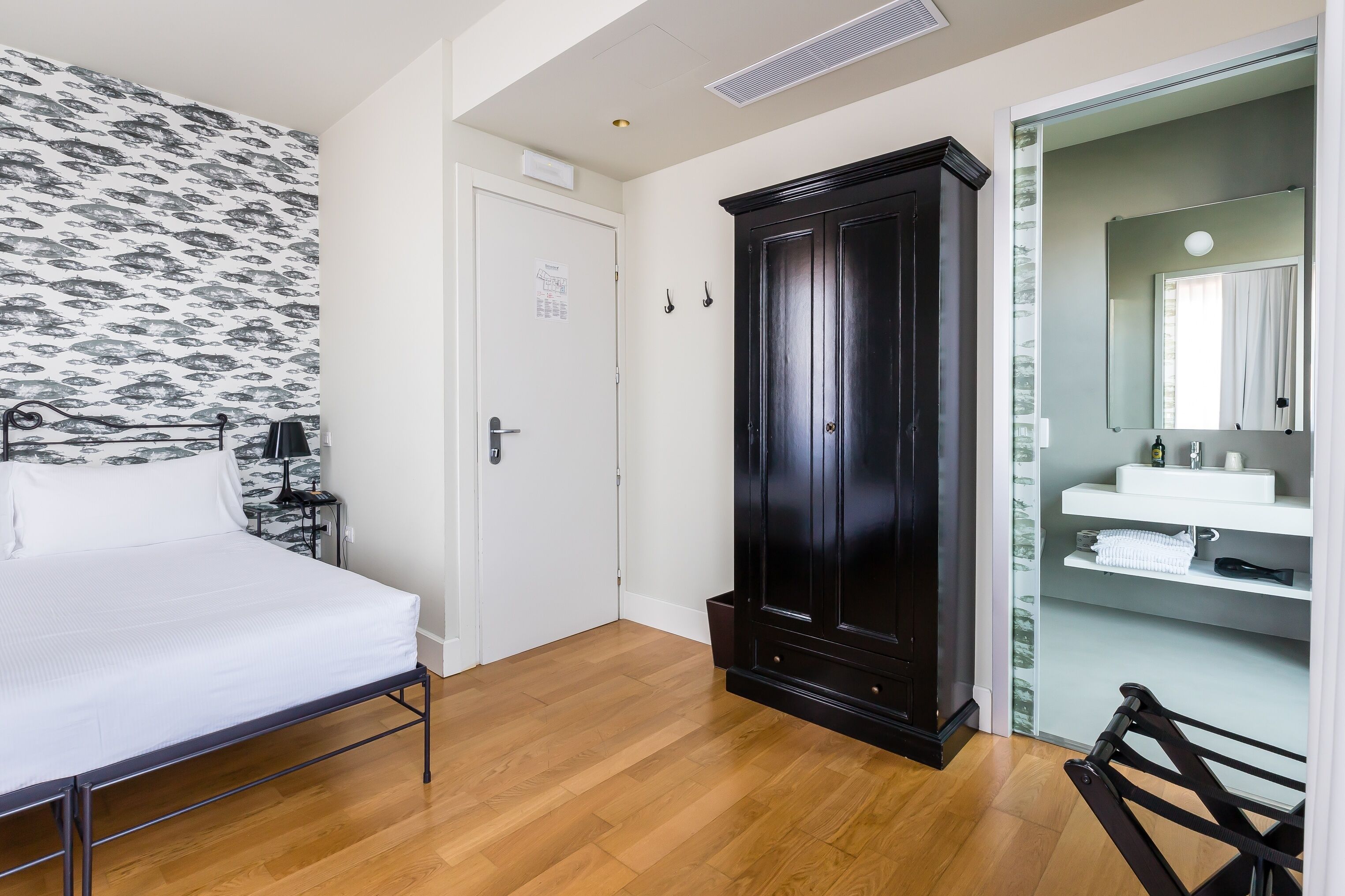 Une chambre à coucher comprenant un lit, une armoire, une salle de bain avec un lavabo et un miroir, et un papier peint à motifs.