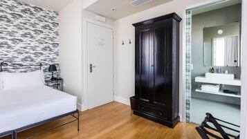 Une chambre à coucher comprenant un lit, une armoire, une salle de bain avec un lavabo et un miroir, et un papier peint à motifs.