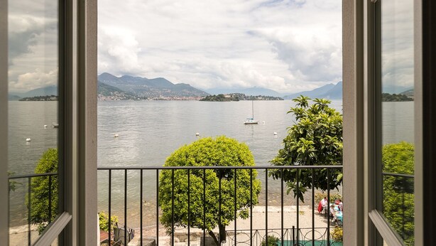 A view of a lake with boats, mountains, and a distant town. - Hotel Belvedere (Stresa)