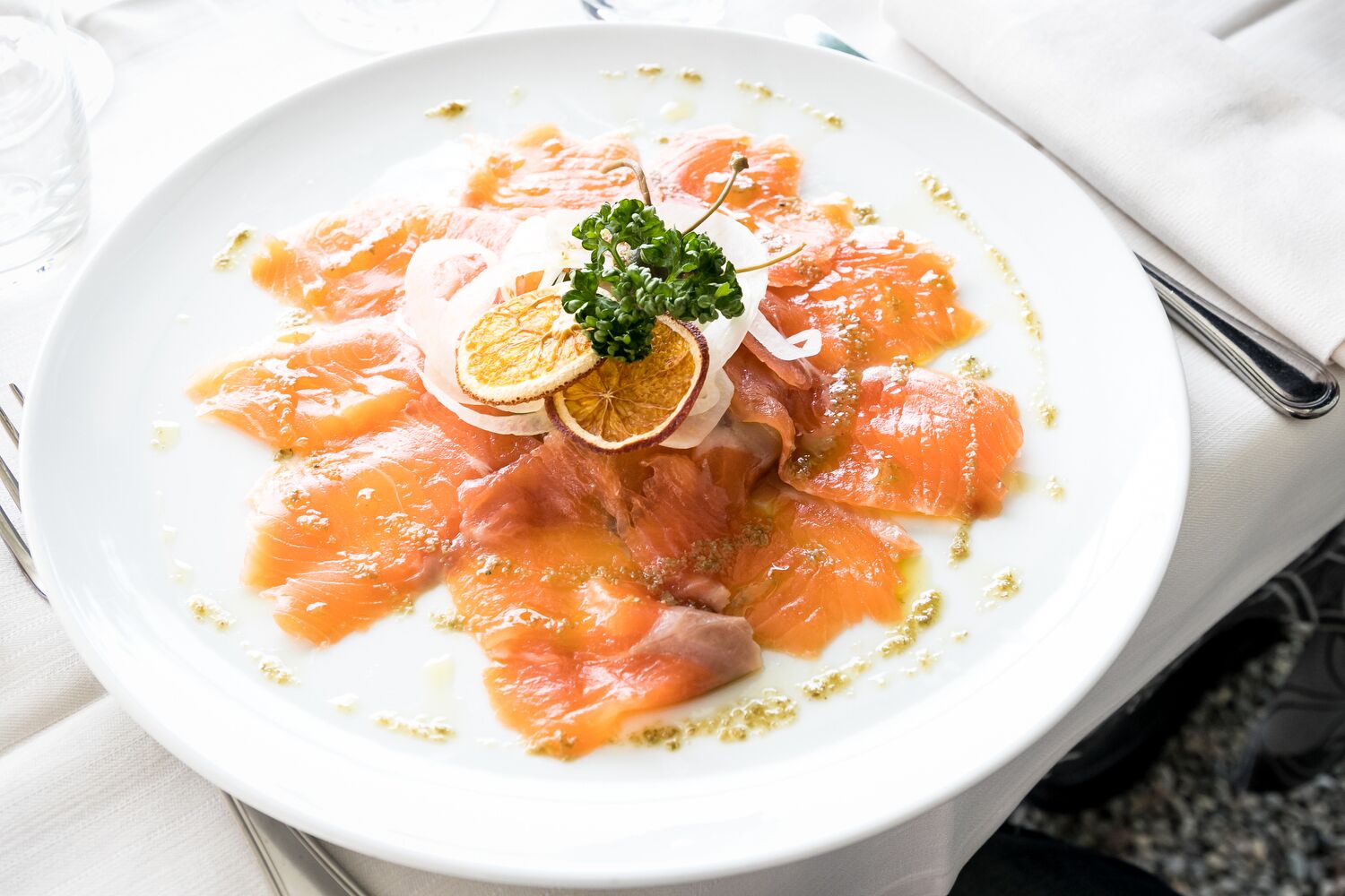 A plate of smoked salmon with lemon slices and a garnish on a white plate.