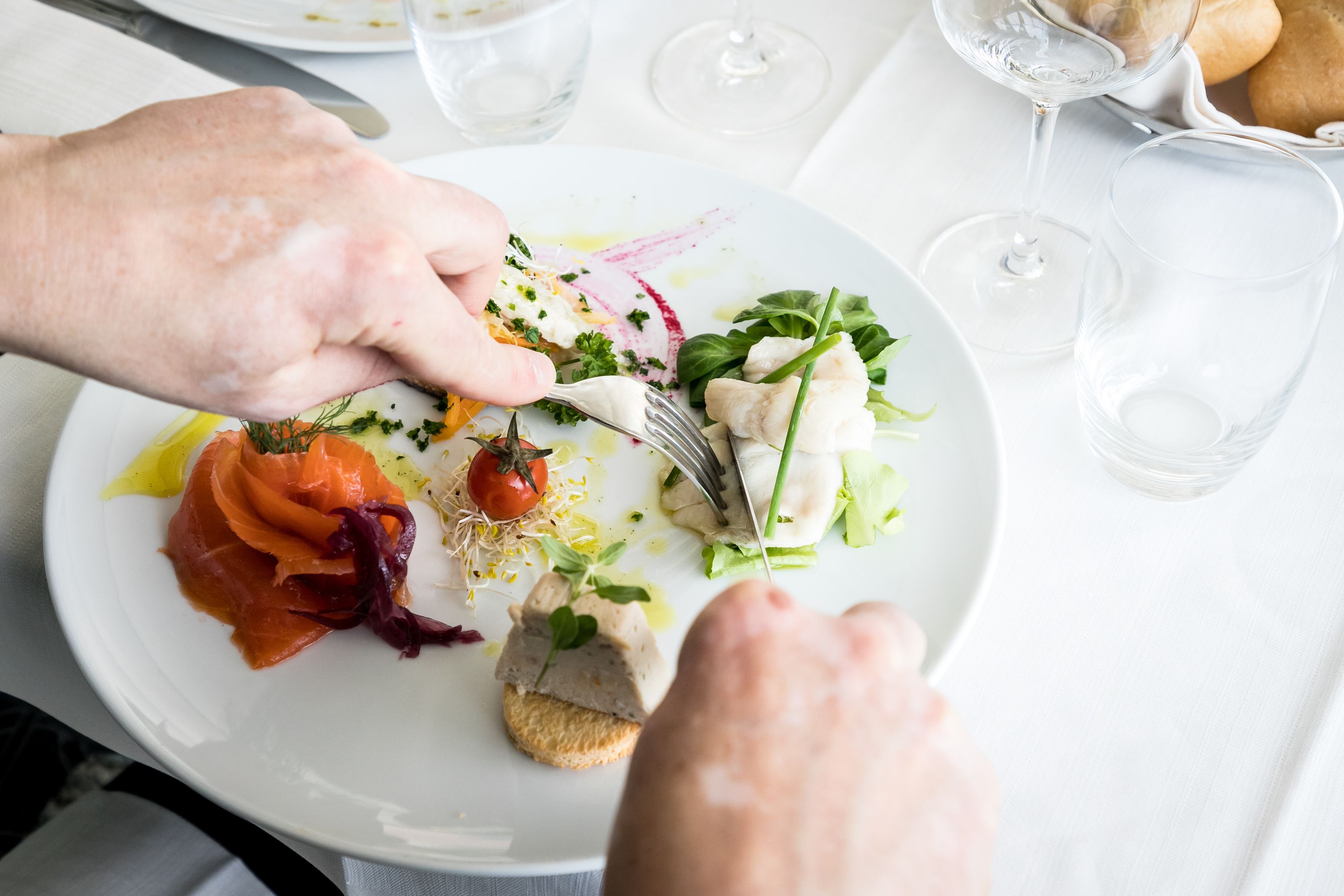 A plate of food with various items including smoked salmon, a piece of fish, and greens, accompanied by a fork.