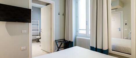 Una habitación de hotel moderna con una cama grande, un televisor de pantalla plana montado en la pared, un radiador y una ventana con cortinas.