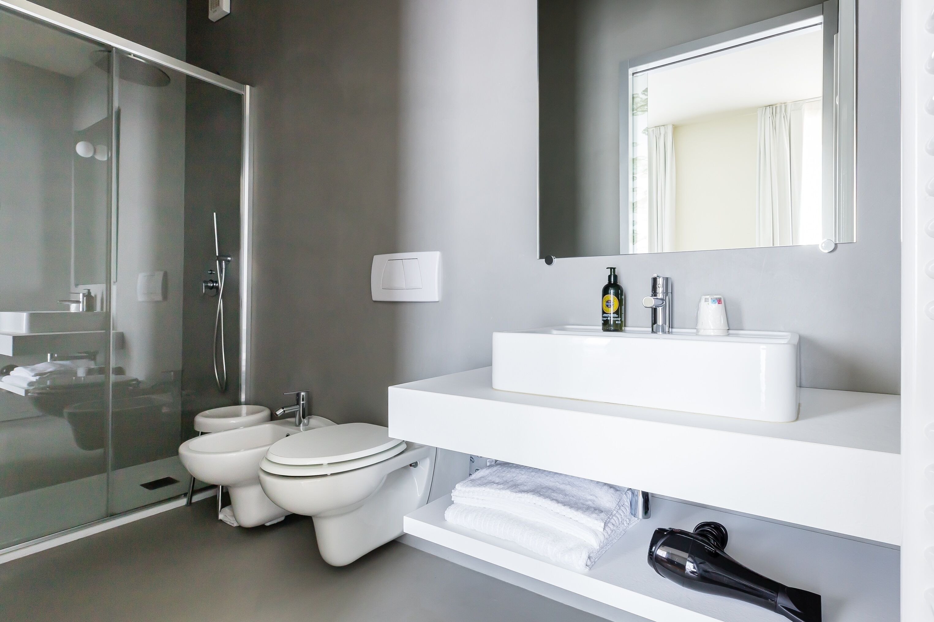Une salle de bain moderne avec une douche à parois de verre, un lavabo blanc avec un miroir au-dessus et des toilettes.