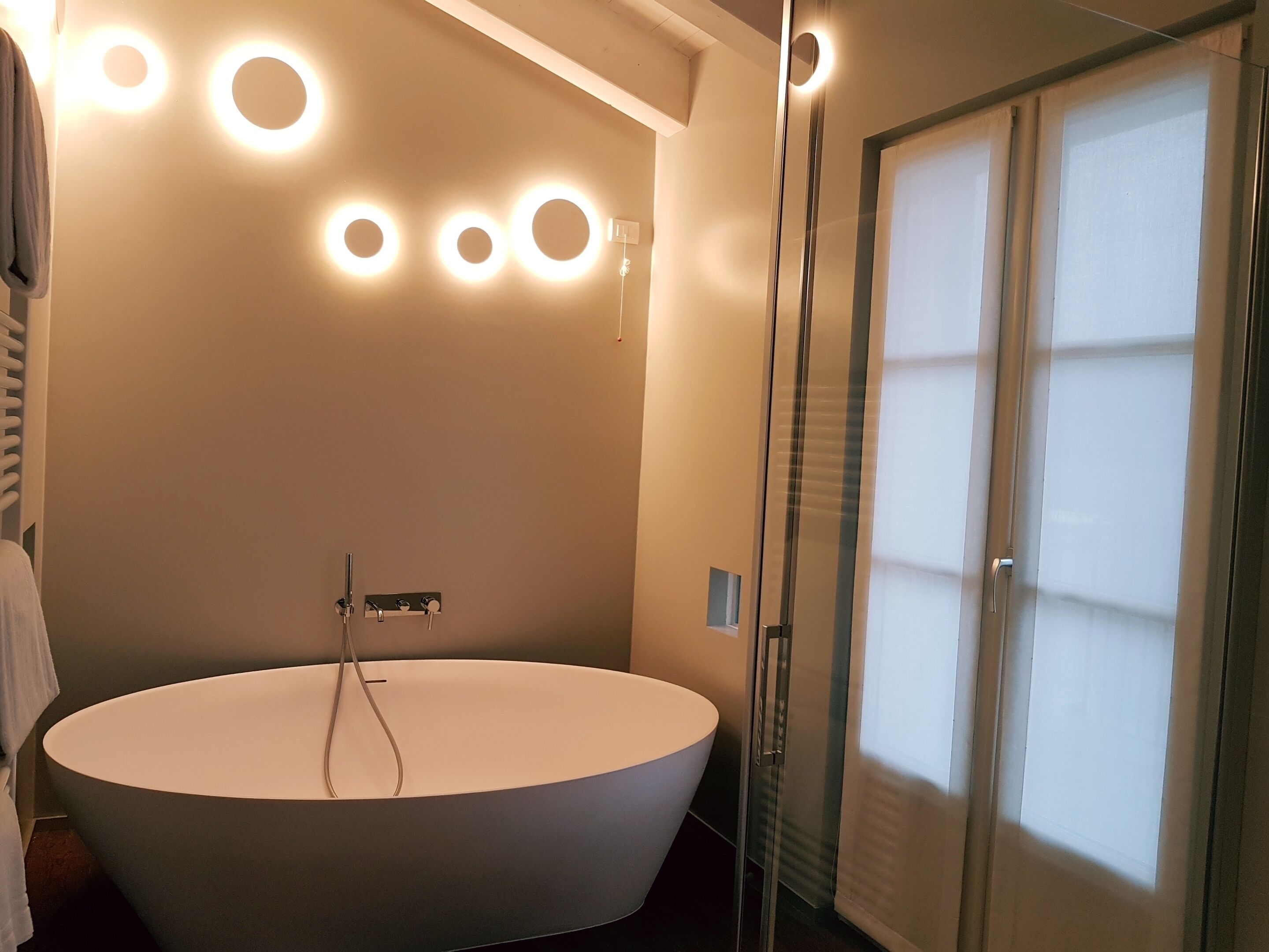A modern bathroom with a freestanding bathtub, circular wall sconces, and a glass shower enclosure.