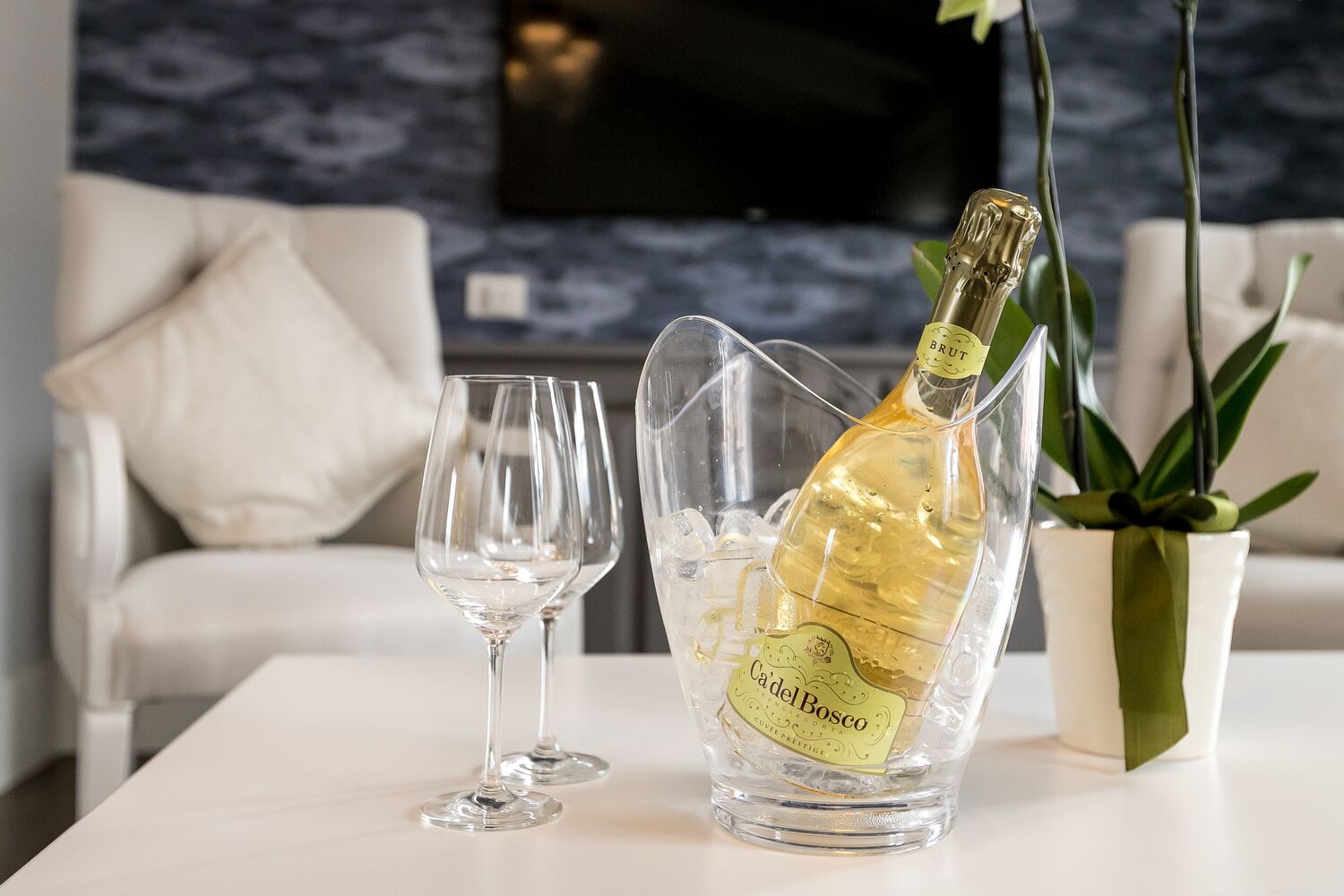 Una botella de champán Brut en un recipiente de vidrio sobre una mesa, acompañada por dos copas de vino vacías.