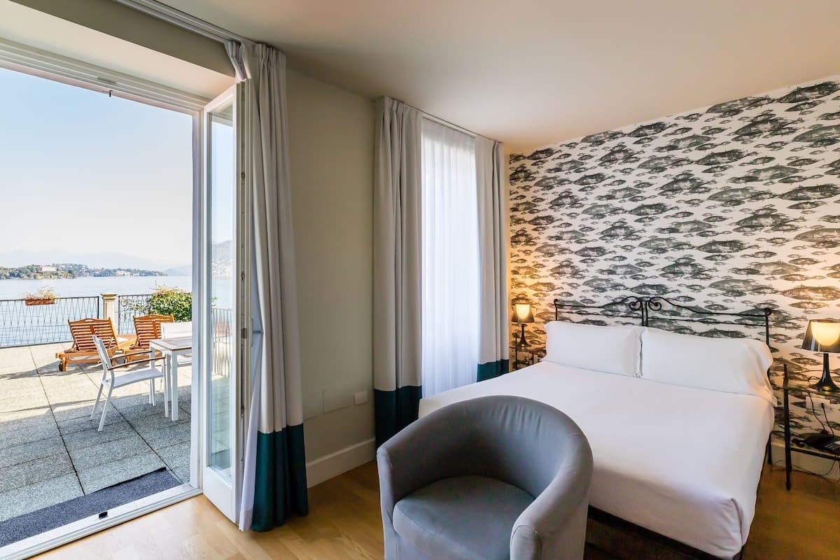 A hotel room with a bed, a chair, a table, and a view of the sea.