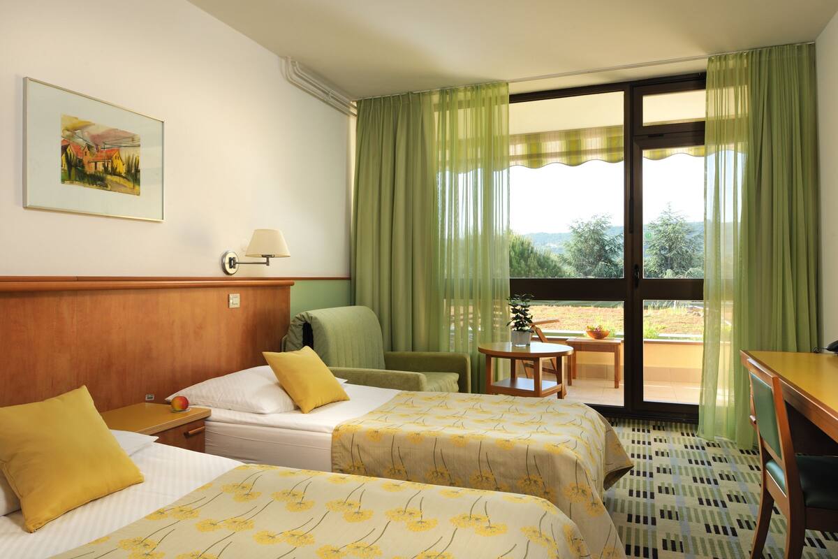 Une chambre d’hôtel avec deux lits, une table, une chaise, une lampe et une vue sur l’extérieur.