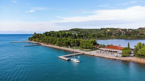 Un pueblo costero con un puerto deportivo, un restaurante con terraza y una colina con edificios.