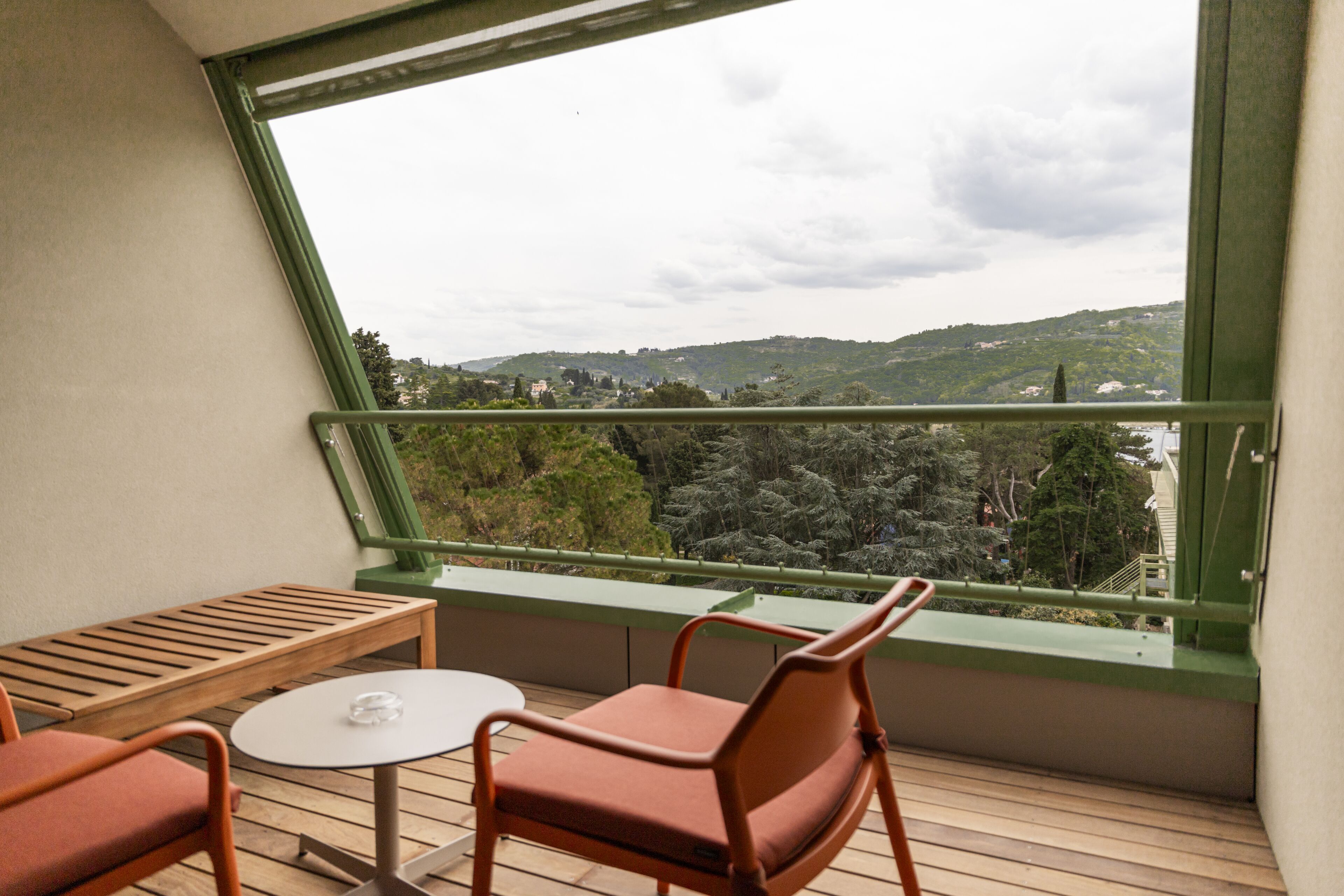 A balcony with a wooden table and two chairs, overlooking a scenic view of hills and trees.