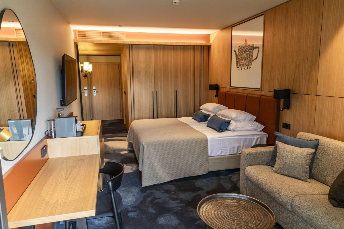 Une chambre d’hôtel moderne équipée d’un lit, d’un canapé, d’un bureau, d’un miroir et d’une armoire.