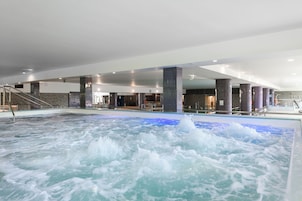 Un amplio espacio interior con jacuzzi y piscina, rodeado de columnas y una escalera.