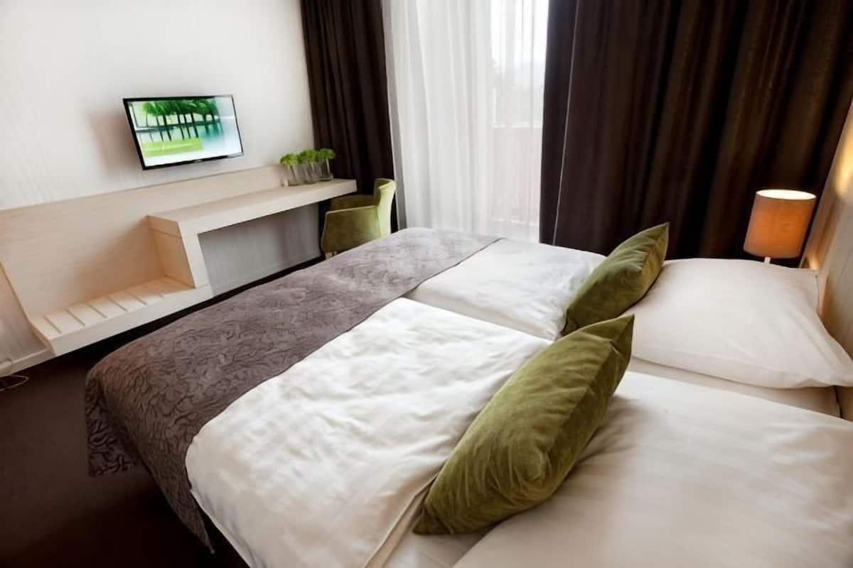 Una habitación de hotel con cama, televisor en la pared, estante con plantas y lámpara.