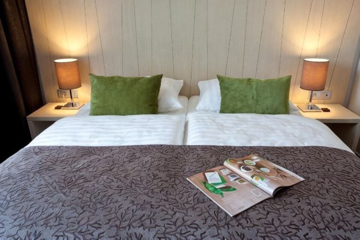 Un lit double avec une couvre-lit à motifs, deux oreillers verts et blancs, et deux lampes de chevet de chaque côté.
