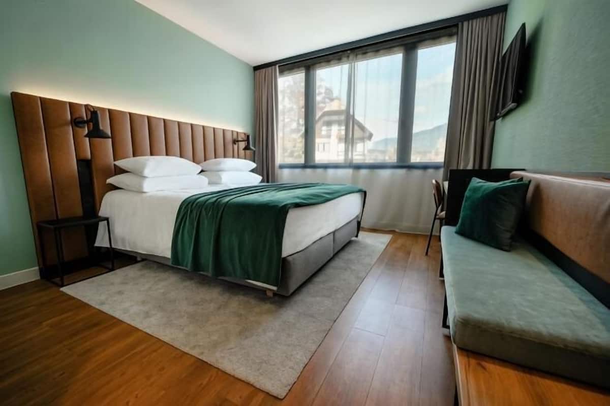 Un dormitorio con cama, sofá, ventana y televisión en la pared.