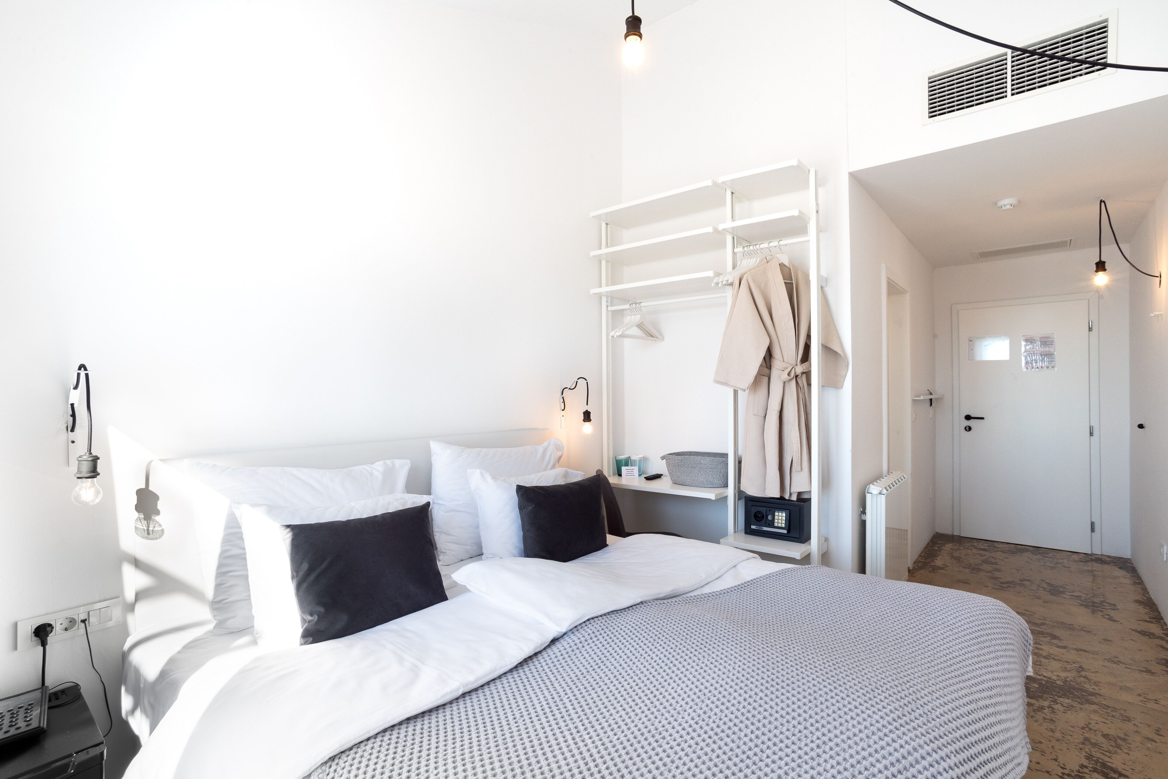 Un dormitorio moderno con una cama bien hecha, un armario blanco y un escritorio pequeño con una lámpara.