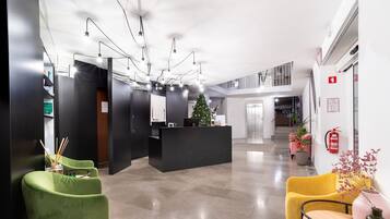 A modern hotel lobby with a reception desk, green and yellow seating, a Christmas tree, and a fire extinguisher on the wall.