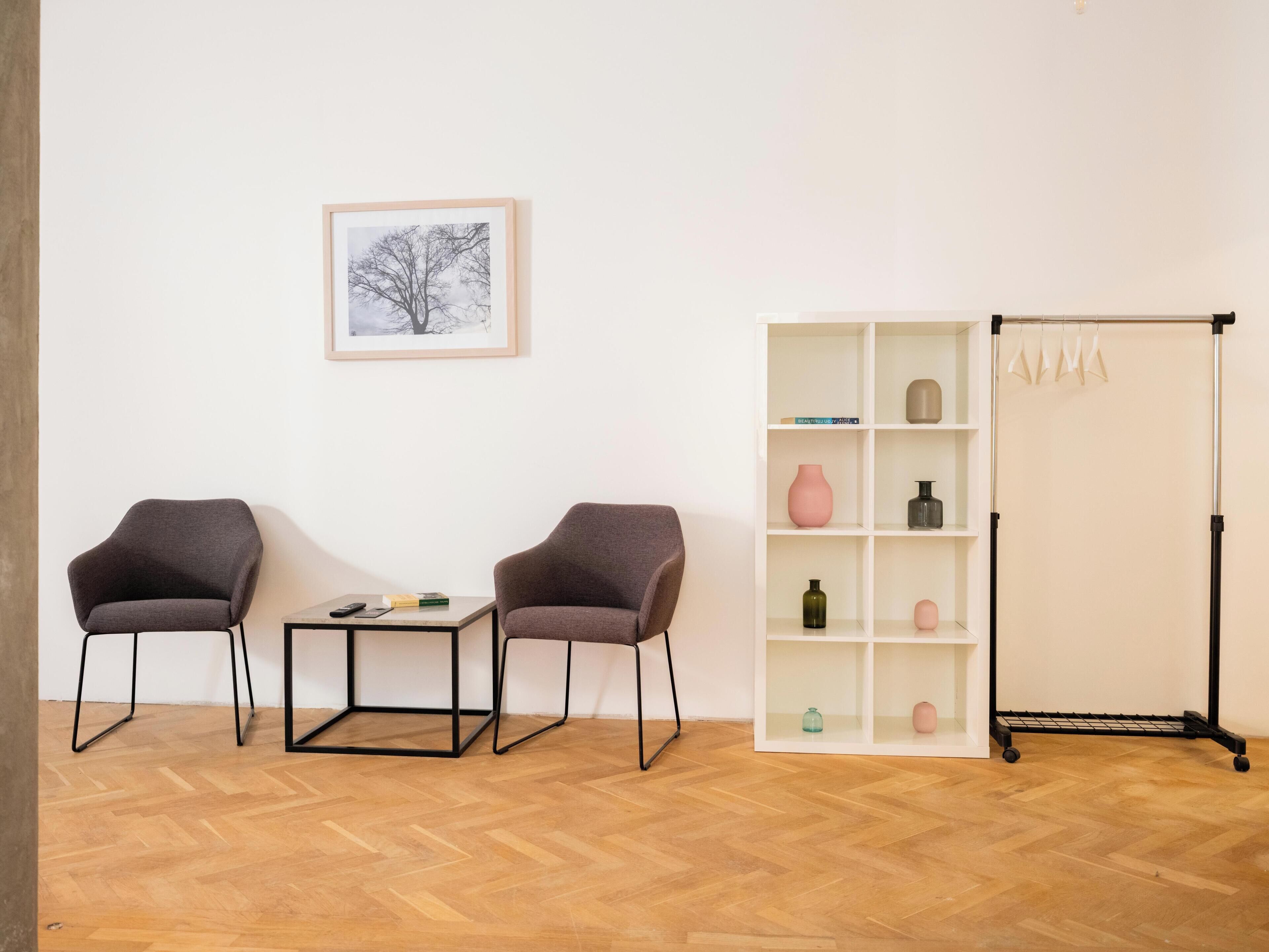 A room with two armchairs, a small table, a white shelving unit with decorative items, and a floor lamp.