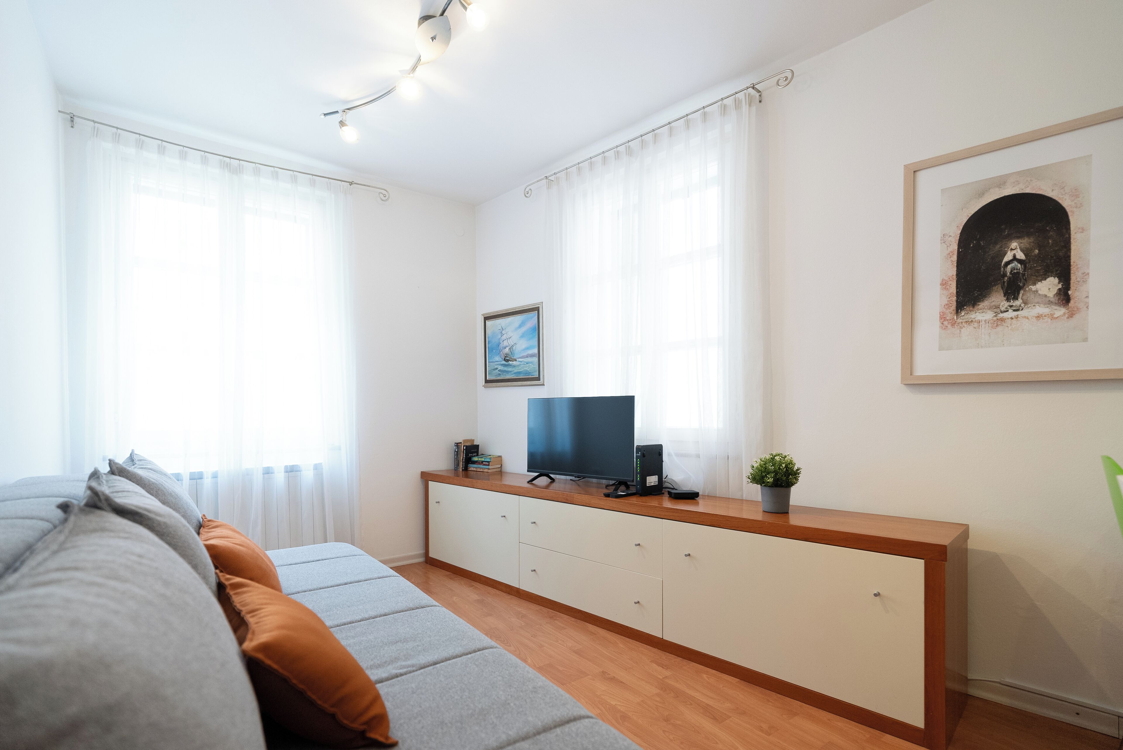 Een moderne slaapkamer met een bank, een televisie op een houten dressoir en kunst aan de muur.