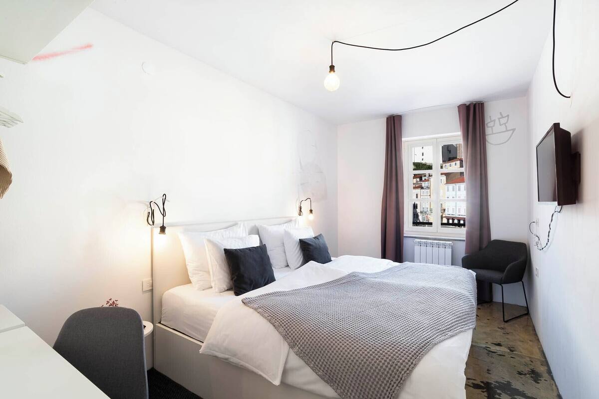 A hotel room with a bed, bedside table, chair, and a TV mounted on the wall.
