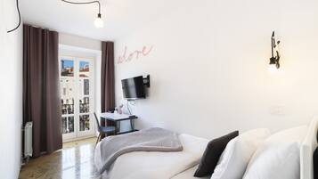 A bedroom with a bed, a desk, a chair, a TV, and a window with curtains.