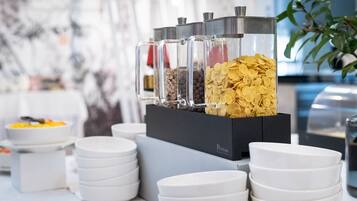 Montaje de bufé con recipientes de vidrio transparente que contienen diversos alimentos, platos blancos apilados sobre una mesa y una caja negra con la etiqueta 'PANTHEA'.