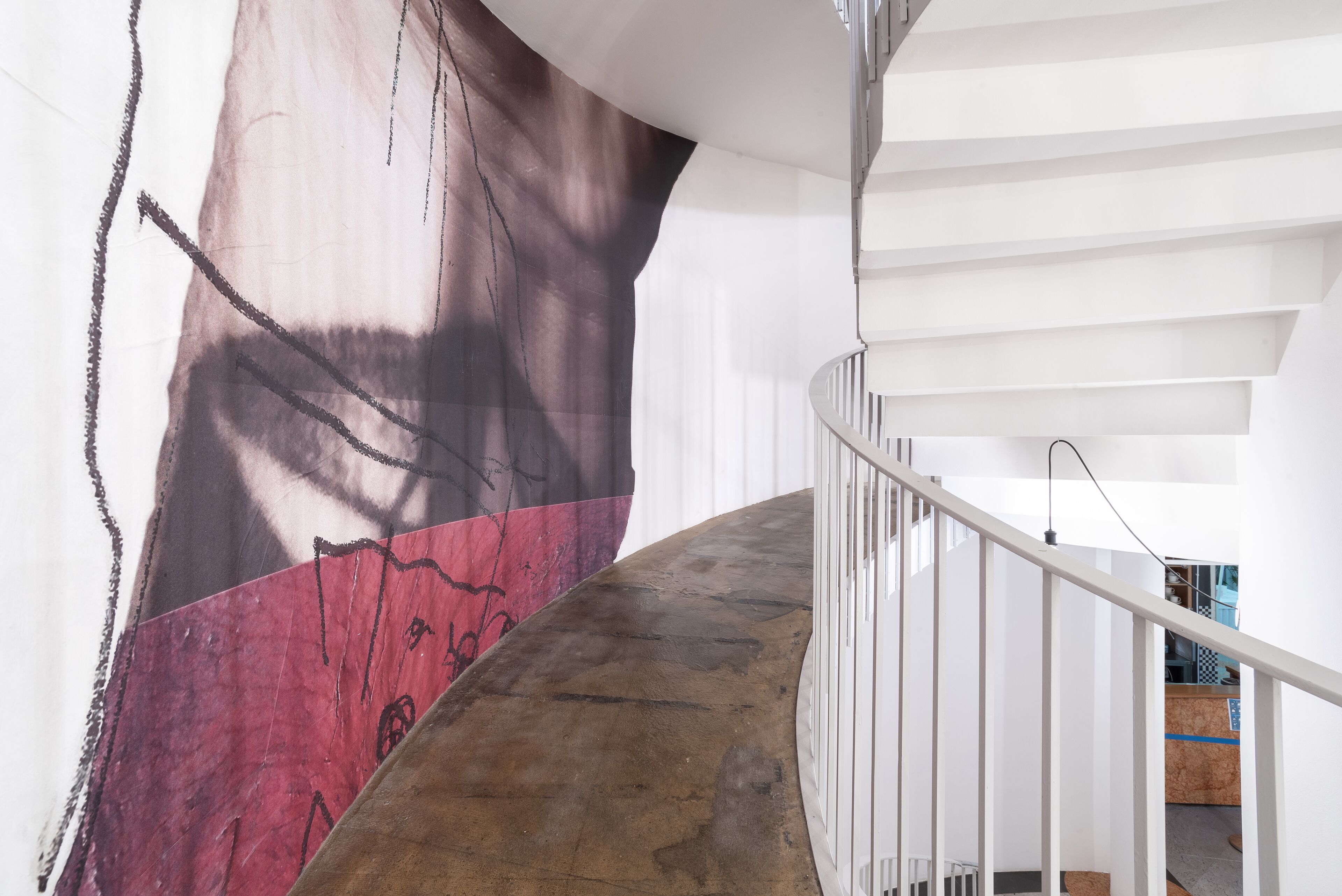 Una escalera con piso de concreto y barandas blancas, que conduce a un cuarto con un gran mural abstracto en la pared.