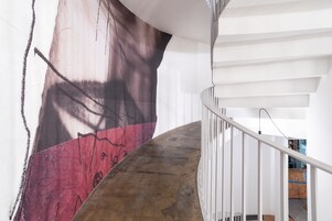 Una escalera con piso de concreto y barandas blancas, que conduce a un cuarto con un gran mural abstracto en la pared.