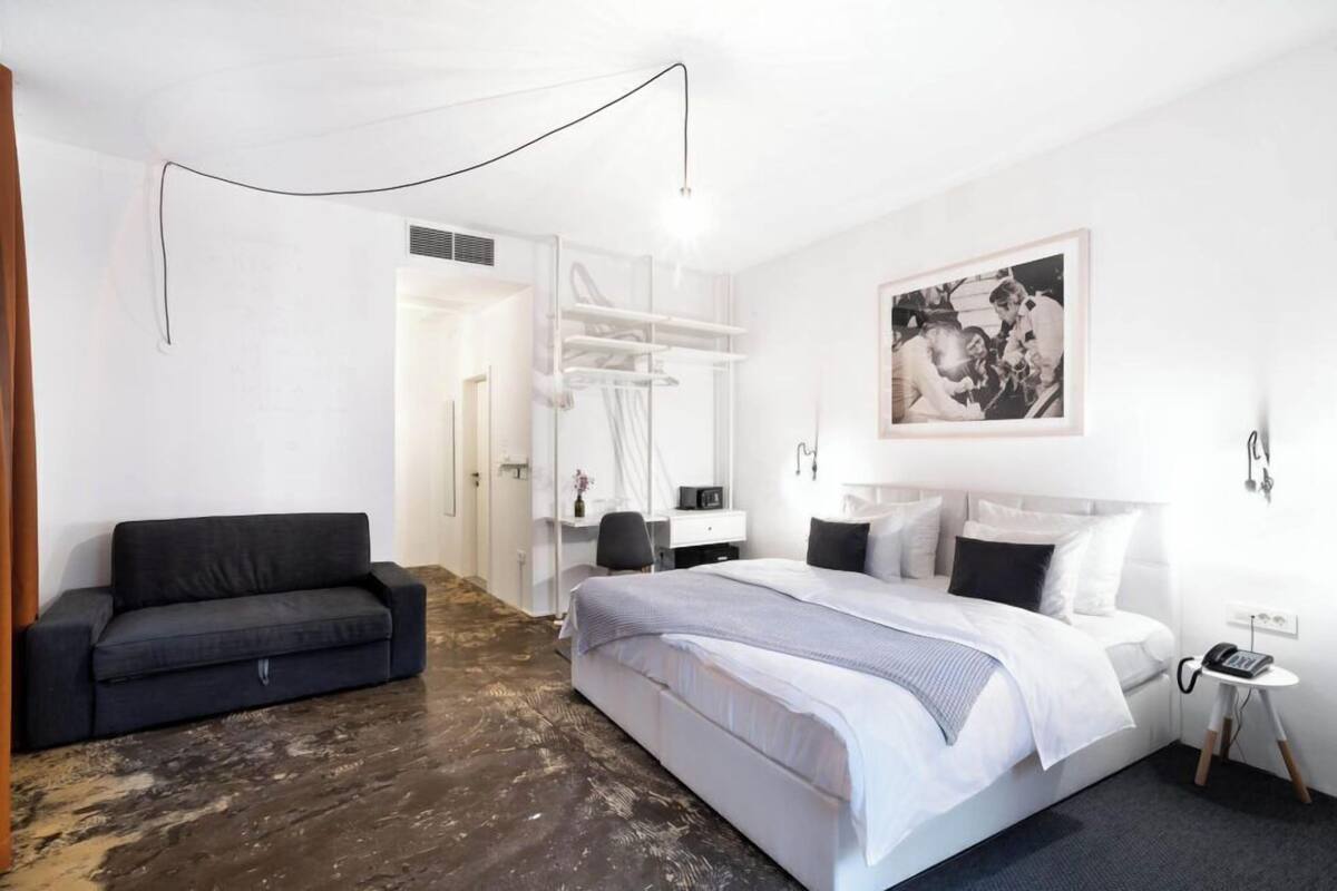 A modern hotel room with a large bed, a sofa, a desk, and a wardrobe.