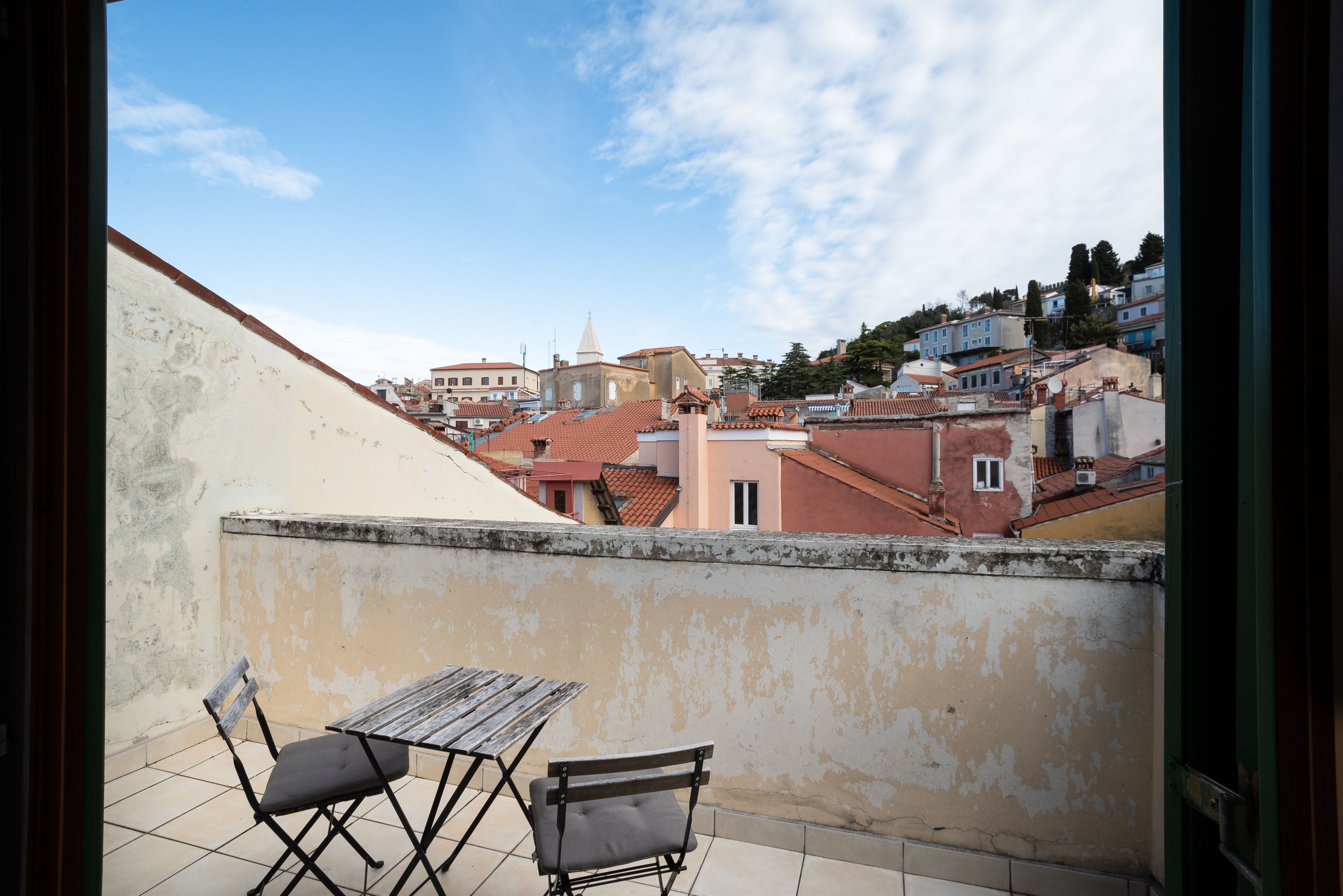 A balcony with a wooden table and chairs, overlooking a cityscape with buildings and a church.