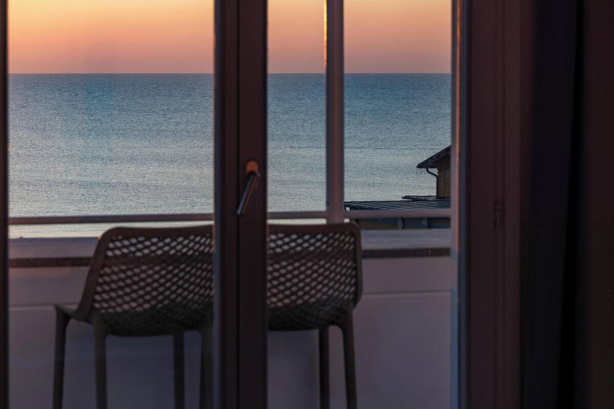 A balcony with a view of the sea, a chair, and a small building structure.