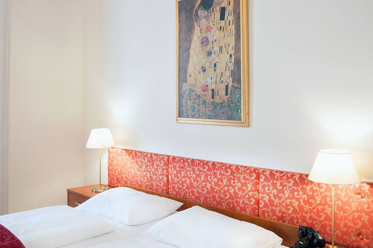 Quarto de hotel com uma cama grande, duas mesas de cabeceira, um quadro clássico e um telefone em uma das mesas.