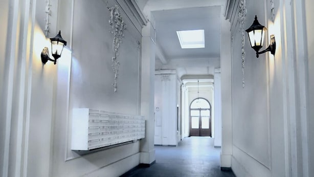 A corridor with white walls, black wall sconces, and a white bench. - Hotel Pension Andreas (Vienna)