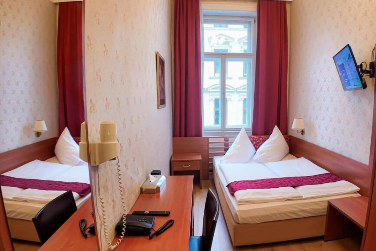 Quarto de hotel com duas camas, uma mesa de trabalho com telefone e uma televisão na parede.