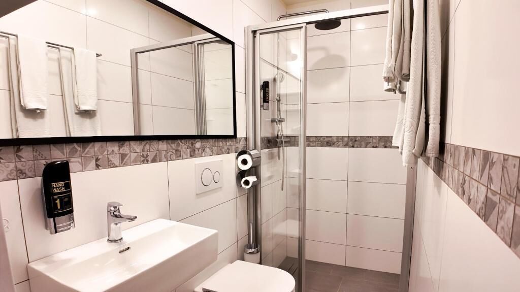 A modern bathroom with a glass shower enclosure, a white sink, and a hand wash station.