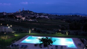 A swimming pool with lounge chairs and a view of a hill with buildings. - Villa Ducci (San Gimignano)