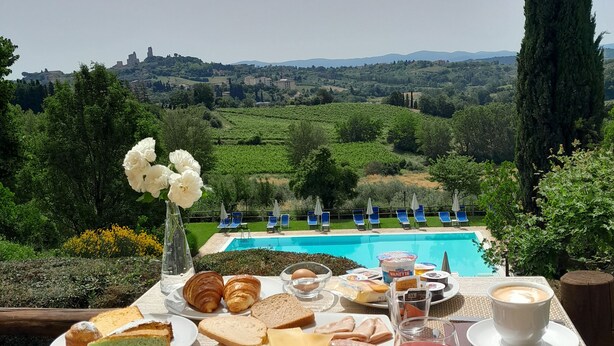 A breakfast table with various foods and a cup of coffee, overlooking a pool and scenic landscape. - Villa Ducci (San Gimignano)