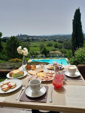 Taula de l'esmorzar amb diversos aliments i una tassa de cafè, amb vista a una piscina i un paisatge idíl·lic.