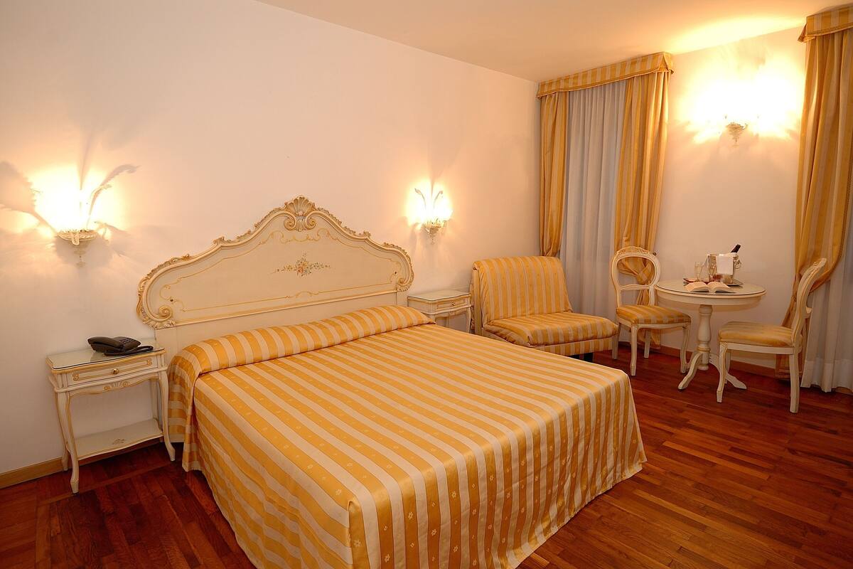 A hotel room with a large bed, two bedside tables, a chair, a small round table, and a mirror.