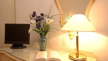 Un bureau avec un écran d’ordinateur, un livre ouvert, un vase de fleurs et une lampe.
