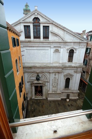 Un edificio storico dall'architettura classica, con un ingresso centrale ornato da una statua, finestre ad arco e una targa con iscrizioni.