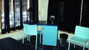 Une pièce comprenant un bureau, deux chaises, une lampe, une poubelle et une fenêtre avec des rideaux.