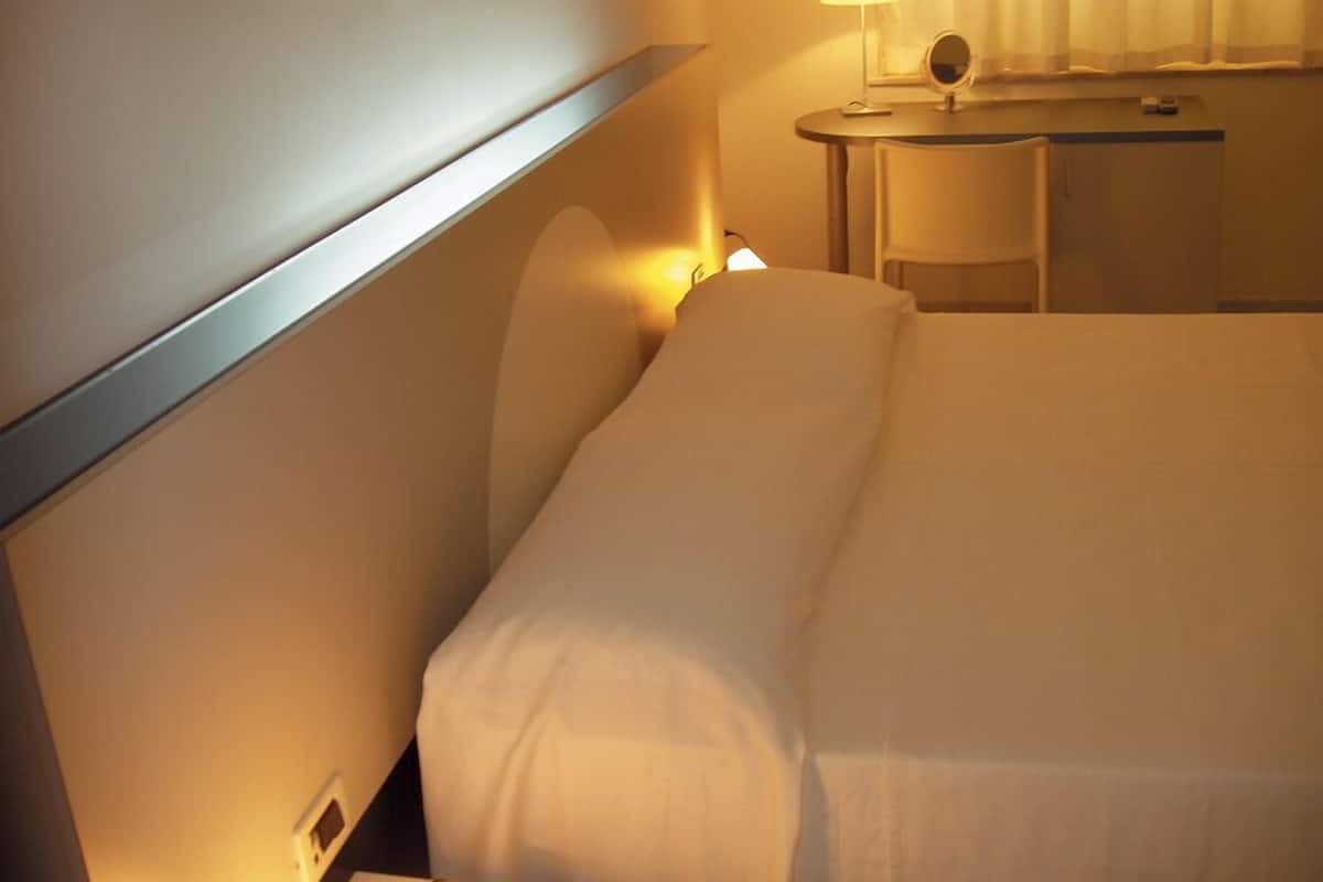 A hotel room with a bed, bedside table, lamp, and a mirror.