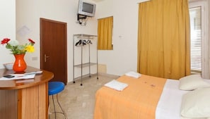 A hotel room with a bed, a desk with a chair, a TV mounted on the wall, and a window with curtains. - Rainbow (Palermo)