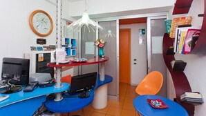 Une pièce avec un bureau, un ordinateur et une chaise. Il y a une horloge au mur et une porte à l’arrière-plan.