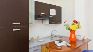 Une cuisine compacte avec un évier, un vase de fleurs et un petit plan de travail sur lequel se trouvent une télécommande et un journal.