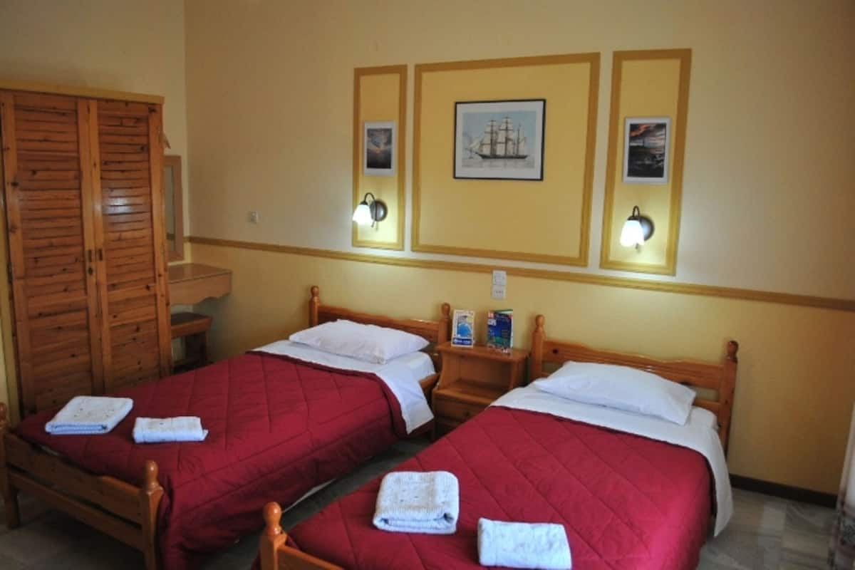 A room with two wooden beds, each with a red quilt and white pillows, and a wooden wardrobe.