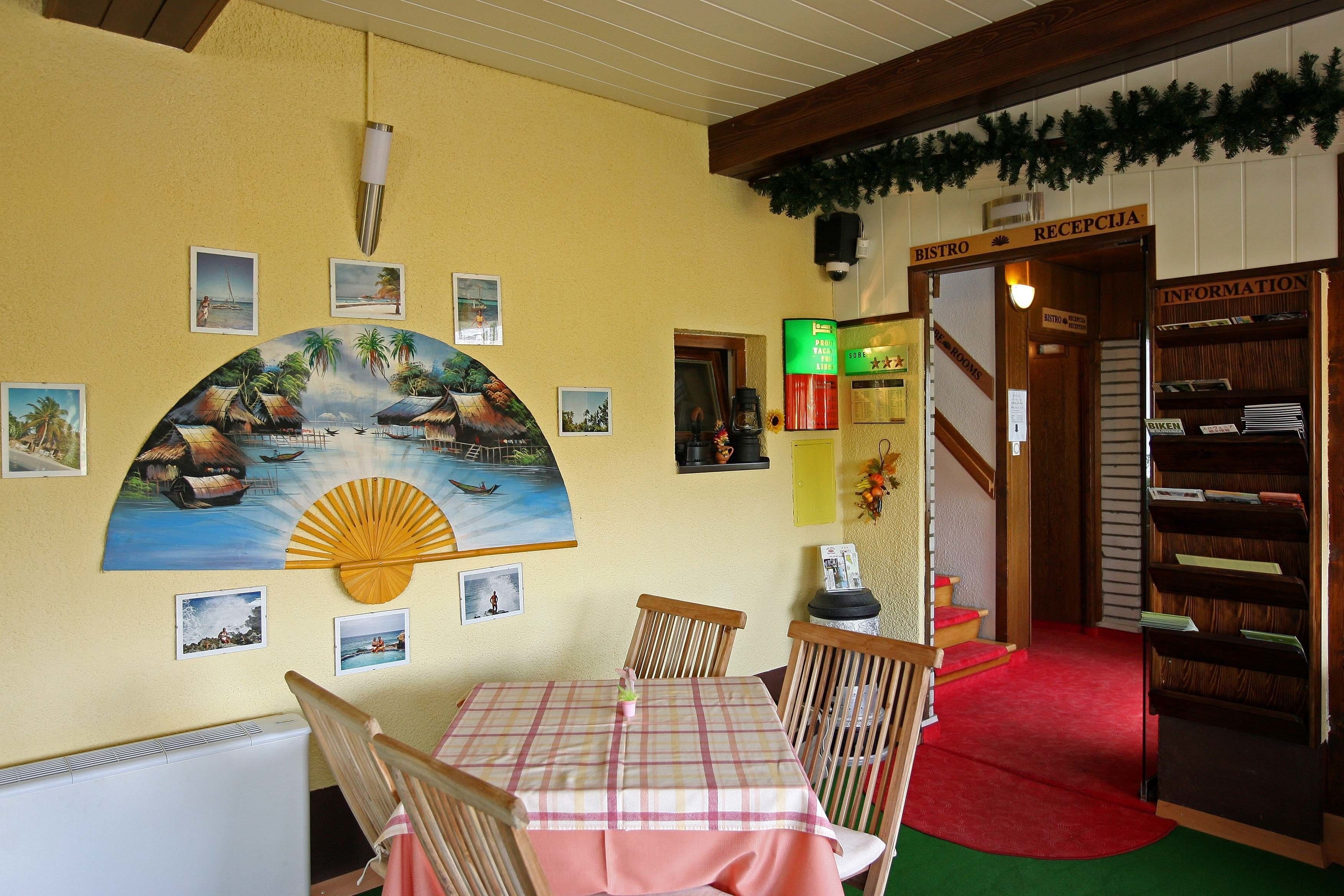 Spiseområde med et bord og stole, et maleri af et tropisk landskab, en receptionsdisk og en trappe til informationsdisken.